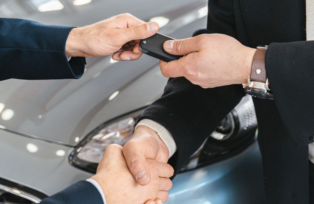 Car keys being handed to a buyer beside a vehicle.